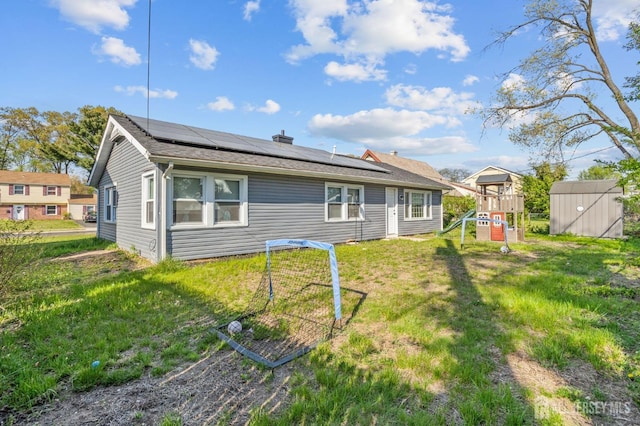 back of property featuring solar panels, an outdoor structure, a lawn, a playground, and a storage unit