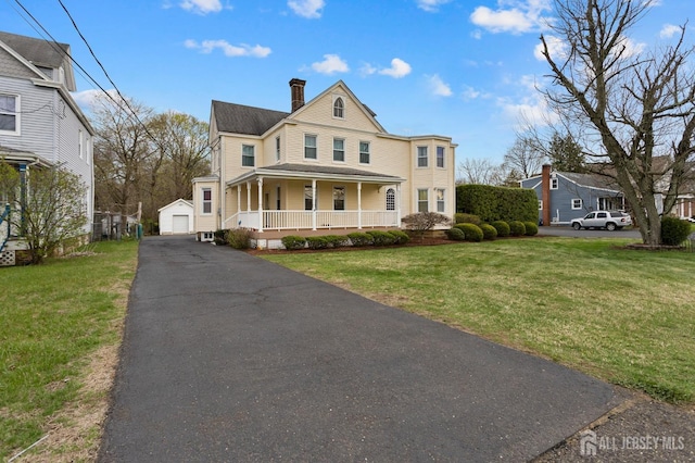 view of front facade with a porch, a front lawn, a chimney, and an outbuilding