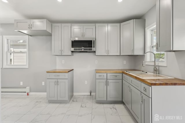 kitchen with stainless steel microwave, butcher block countertops, baseboard heating, a sink, and recessed lighting