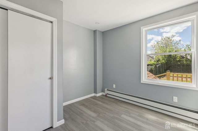 unfurnished bedroom featuring a baseboard radiator, wood finished floors, baseboards, and a closet
