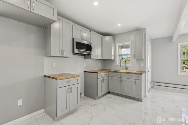 kitchen featuring wood counters, stainless steel microwave, a sink, a baseboard heating unit, and light marble finish flooring