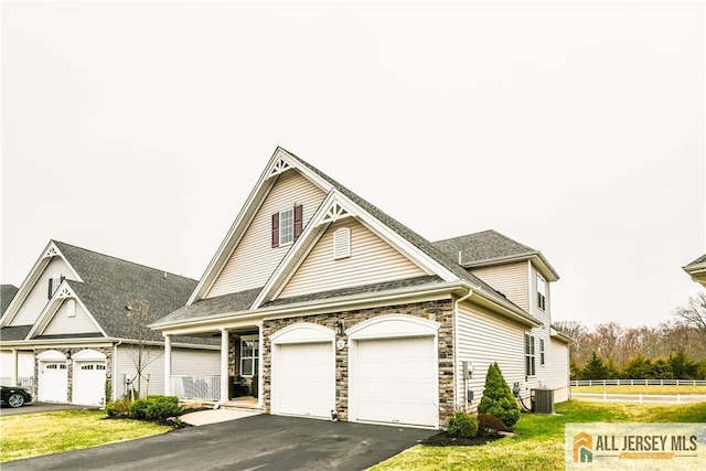 view of front of property with central air condition unit, stone siding, fence, a garage, and aphalt driveway