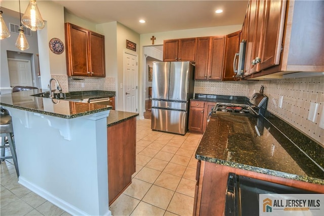 kitchen featuring stainless steel appliances, dark stone countertops, a sink, decorative backsplash, and a peninsula