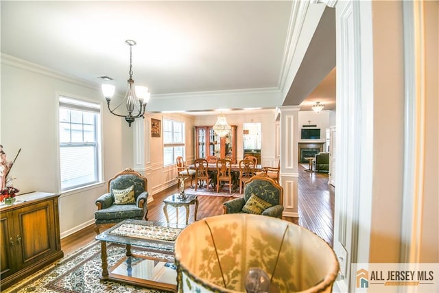 dining area with dark wood finished floors, decorative columns, a notable chandelier, crown molding, and a fireplace