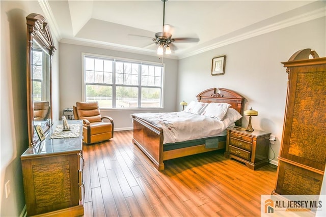 bedroom featuring a raised ceiling, wood finished floors, ornamental molding, baseboards, and ceiling fan