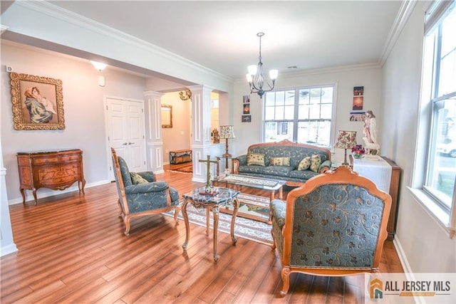 living room with crown molding, a notable chandelier, wood finished floors, and ornate columns