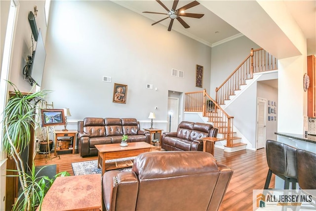 living room with stairway, a towering ceiling, wood finished floors, visible vents, and a ceiling fan