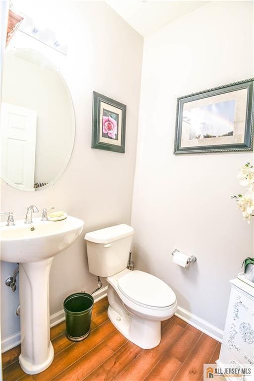 half bath with baseboards, wood finished floors, and toilet