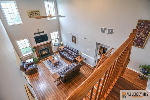 living area with a fireplace with flush hearth, a high ceiling, wood finished floors, and visible vents