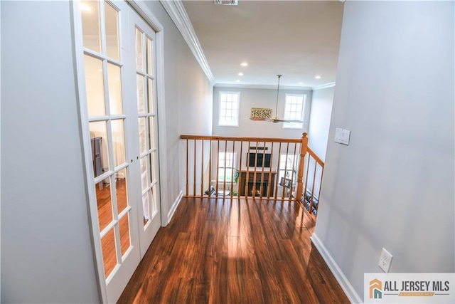 corridor featuring an upstairs landing, wood finished floors, baseboards, ornamental molding, and visible vents