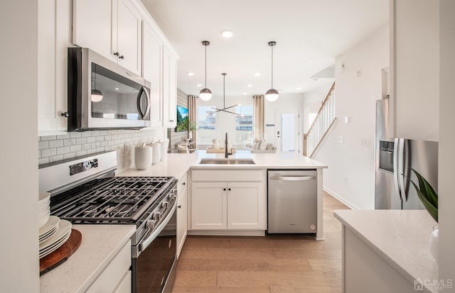 kitchen featuring a sink, stainless steel appliances, white cabinetry, a peninsula, and backsplash
