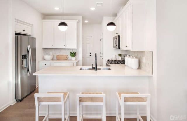 kitchen featuring a sink, stainless steel appliances, white cabinetry, a peninsula, and decorative backsplash