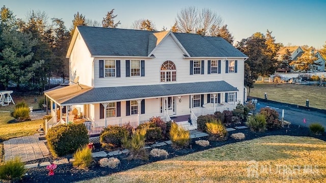 farmhouse-style home featuring a shingled roof, covered porch, and a front lawn