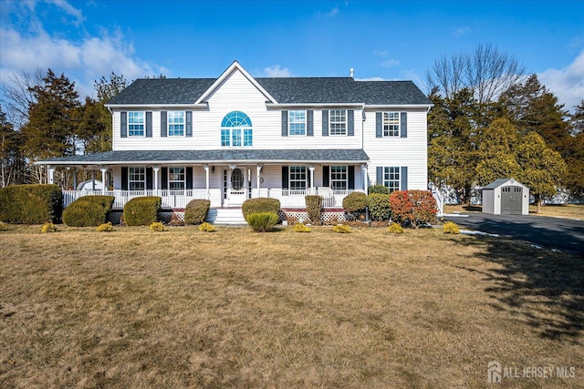 colonial inspired home featuring covered porch, an outdoor structure, roof with shingles, a shed, and a front yard