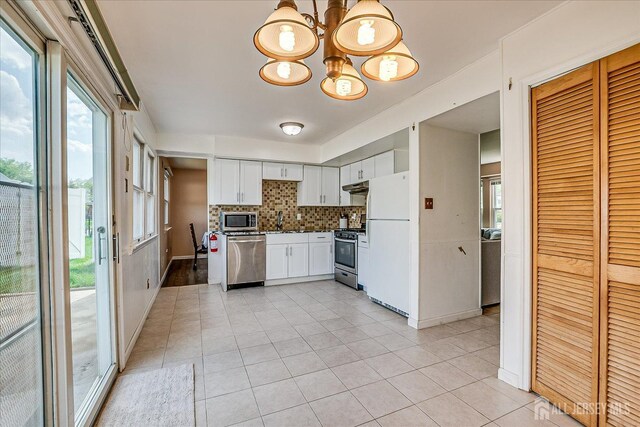 kitchen with stainless steel appliances, a chandelier, light tile patterned floors, decorative backsplash, and under cabinet range hood