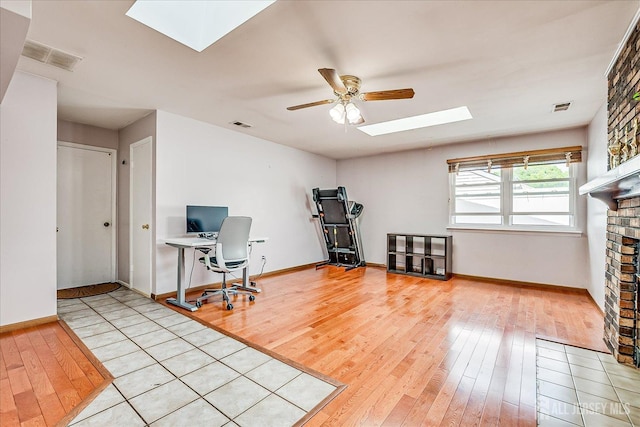 office space with a skylight, hardwood / wood-style flooring, ceiling fan, baseboards, and a brick fireplace