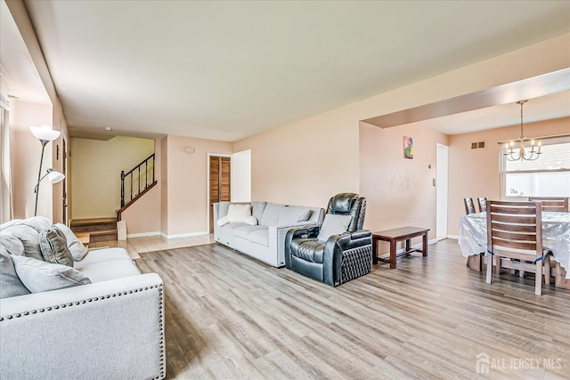 living room featuring light wood-type flooring, stairway, baseboards, and a chandelier