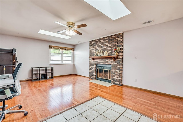 unfurnished office with a skylight, ceiling fan, light wood-style floors, a brick fireplace, and baseboards
