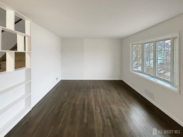 empty room featuring baseboards and dark wood-type flooring