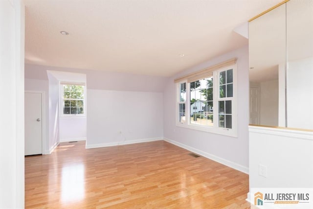 empty room with light wood finished floors, visible vents, and baseboards