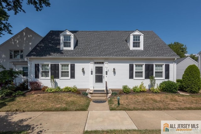 new england style home featuring entry steps, a front yard, and a shingled roof