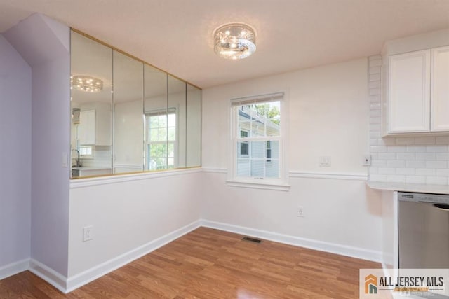 unfurnished dining area featuring a sink, light wood-style floors, visible vents, and baseboards