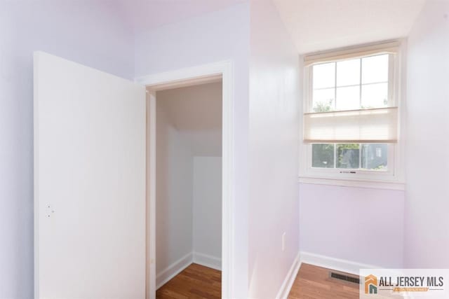 hall featuring baseboards, visible vents, and wood finished floors