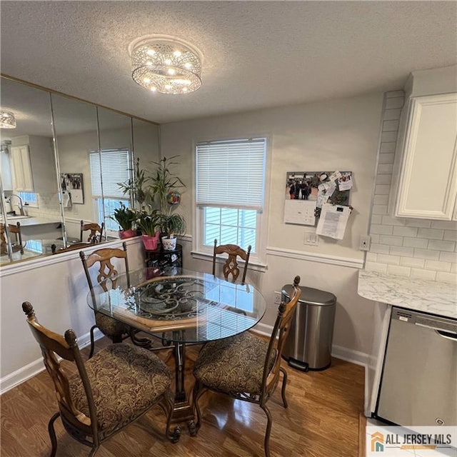 dining space featuring baseboards, a textured ceiling, wood finished floors, and a notable chandelier