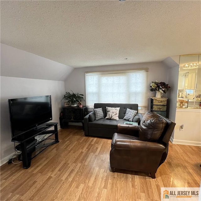 living area featuring baseboards, light wood-type flooring, a textured ceiling, and lofted ceiling