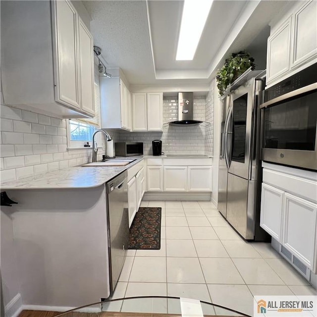 kitchen with wall chimney range hood, a sink, light countertops, stainless steel appliances, and backsplash