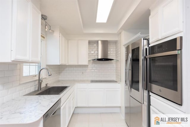 kitchen featuring stainless steel appliances, a sink, white cabinetry, wall chimney exhaust hood, and backsplash