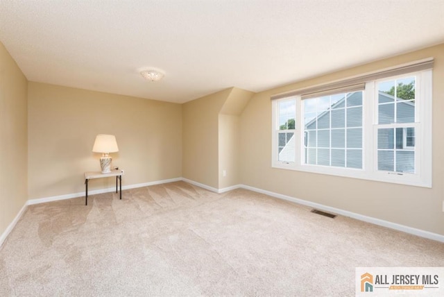 spare room featuring light carpet, visible vents, a textured ceiling, and baseboards