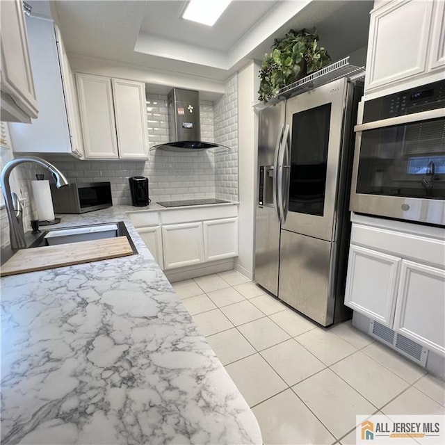 kitchen featuring decorative backsplash, wall chimney exhaust hood, white cabinetry, a sink, and appliances with stainless steel finishes