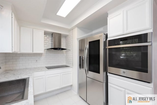 kitchen featuring backsplash, wall chimney range hood, a tray ceiling, stainless steel appliances, and a sink