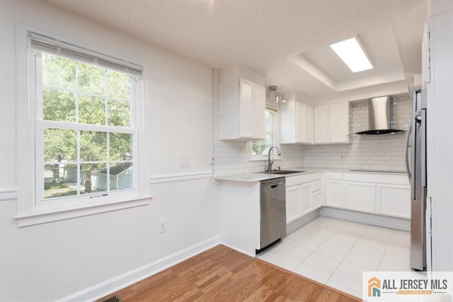 kitchen featuring a sink, backsplash, stainless steel appliances, wall chimney exhaust hood, and white cabinets