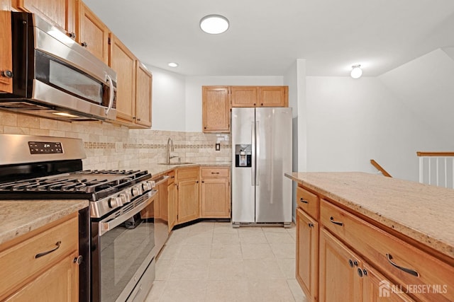 kitchen with light tile patterned floors, light stone counters, a sink, stainless steel appliances, and backsplash