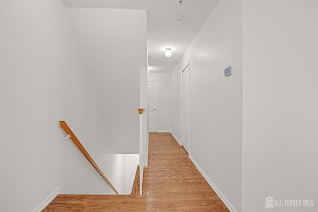 hall featuring light wood-type flooring, baseboards, and an upstairs landing