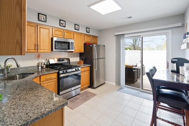 938 Thomas Ave, North Brunswick, NJ 08902 - kitchen with stainless steel appliances, a sink, dark stone counters, light tile patterned floors, and baseboards