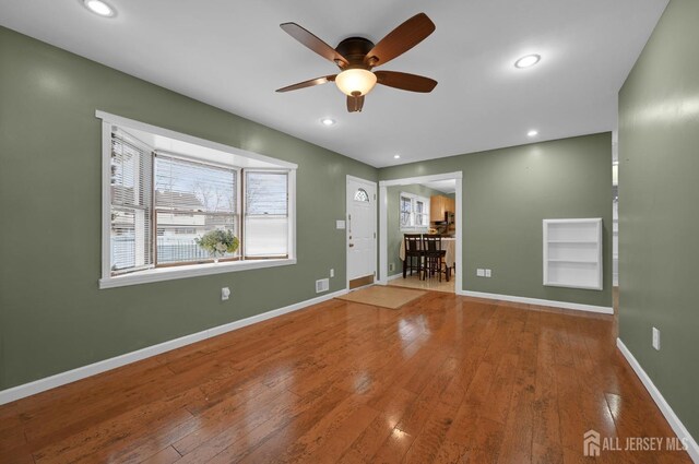 unfurnished living room featuring ceiling fan, built in shelves, and hardwood / wood-style flooring