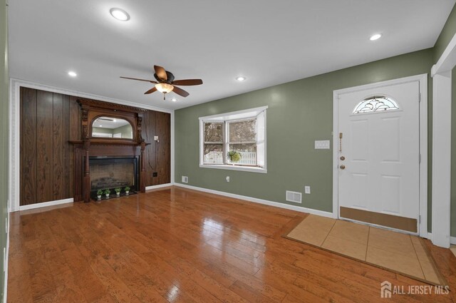 entryway with ceiling fan, wood-type flooring, a fireplace, and wooden walls