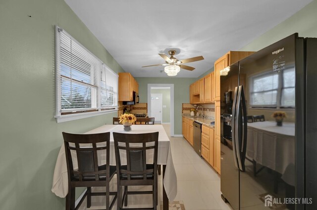 kitchen featuring dishwashing machine, light brown cabinets, black fridge, light tile patterned flooring, and ceiling fan