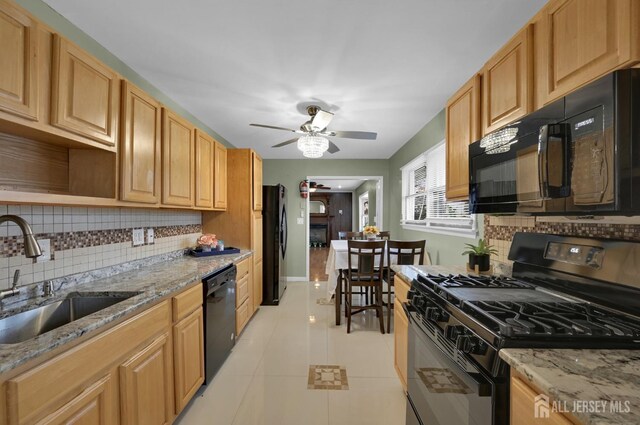 kitchen with light stone countertops, black appliances, sink, ceiling fan, and light tile patterned floors