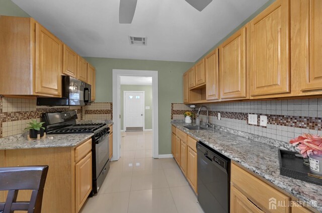 kitchen with light tile patterned floors, light brown cabinetry, light stone countertops, black appliances, and sink