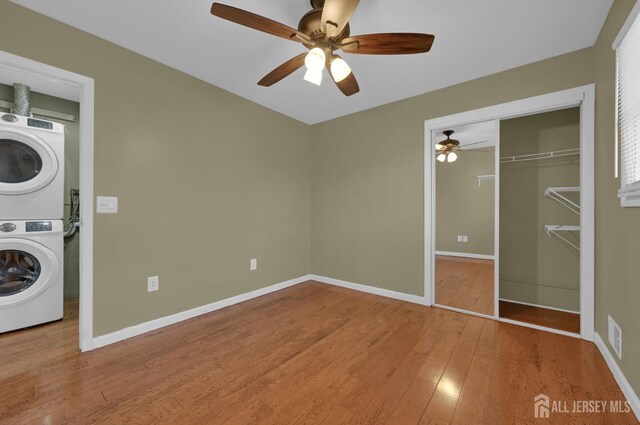 unfurnished bedroom featuring ceiling fan, stacked washer and dryer, a closet, and wood-type flooring