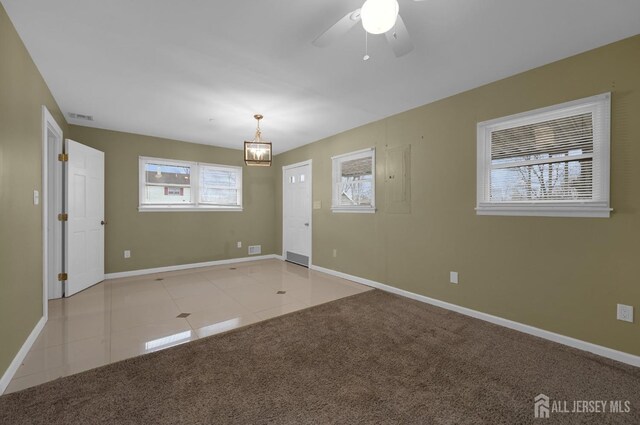 tiled spare room with ceiling fan with notable chandelier and a healthy amount of sunlight