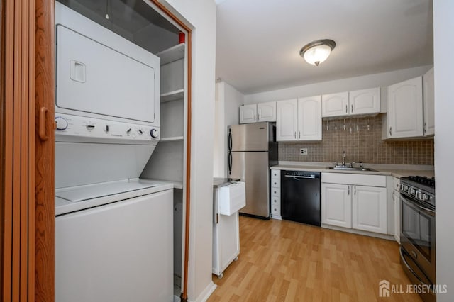 kitchen with stainless steel appliances, stacked washer and dryer, light countertops, white cabinetry, and a sink