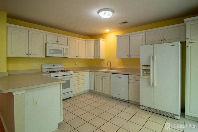 kitchen with white appliances, a sink, a peninsula, light countertops, and light tile patterned floors