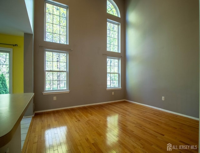 unfurnished living room with light wood-style flooring, a towering ceiling, and baseboards