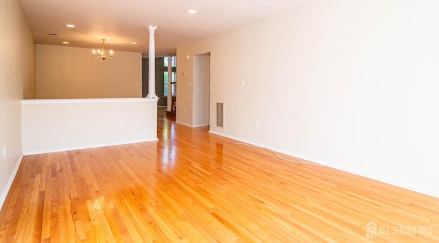 empty room with a chandelier, light wood-style floors, recessed lighting, baseboards, and ornate columns