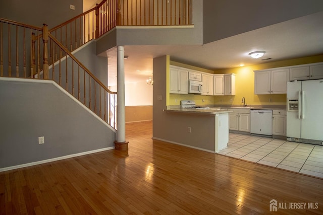 kitchen featuring white appliances, light wood finished floors, a sink, a peninsula, and white cabinetry
